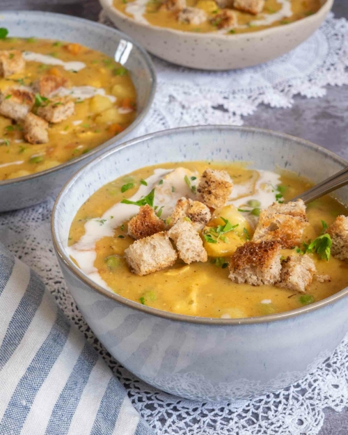 An up close photograph of a bowl of warming vegan creamy chicken soup, topped with crunchy garlic croutons, a swirl of dairy free cream and fresh herbs.