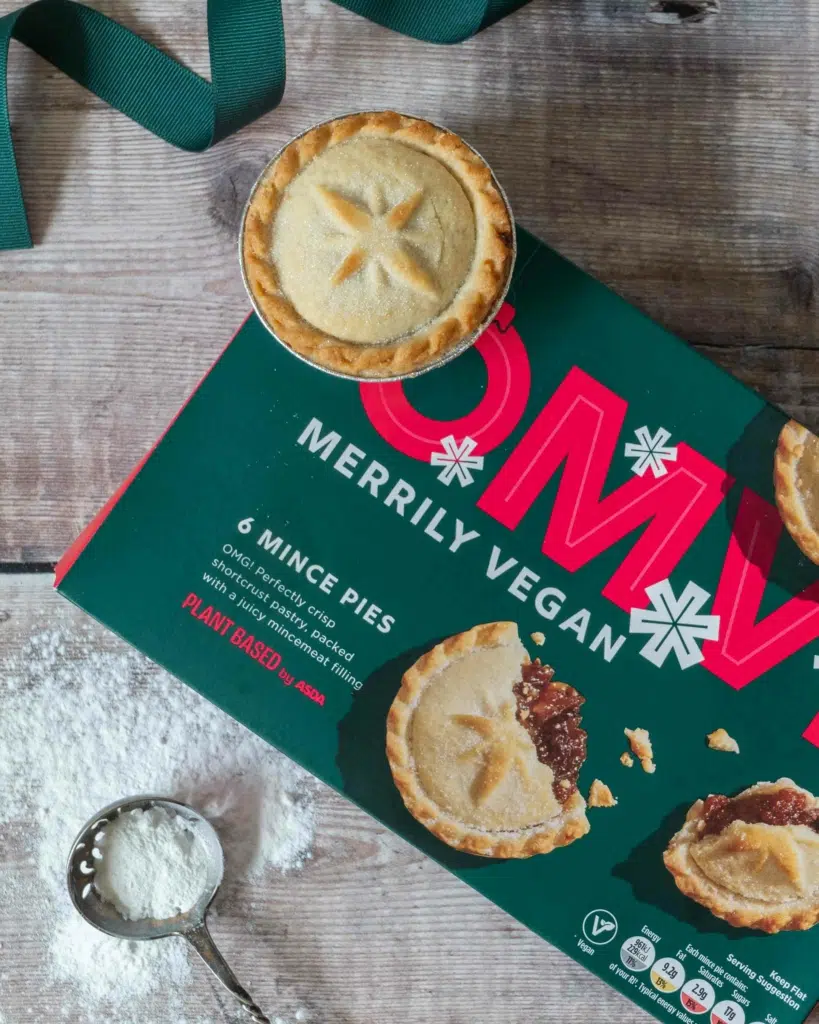 A box of Asda OMV vegan mince pies on a wooden tabletop adorned with green ribbon and icing sugar