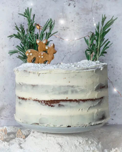 A vegan gingerbread Christmas cake with naked lemon icing, gingerbread deer and rosemary trees
