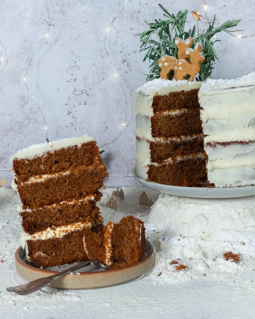 A large slice of vegan gingerbread Christmas cake with naked lemon icing, gingerbread deer and rosemary trees