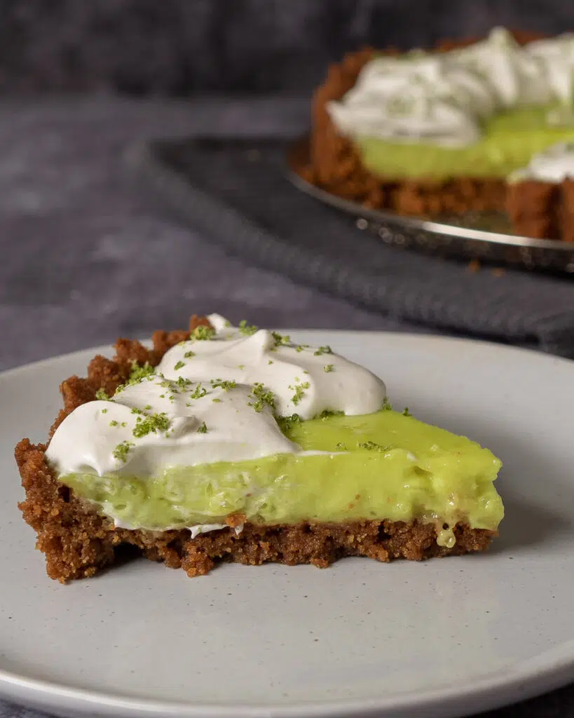 A slice of vegan key lime pie with a ginger nut base, tangy green lime filling and whipped cream on top