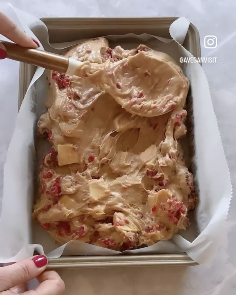 The batter from the white chocolate and raspberry blondie recipe being smoothed into a brownie pan ready to be baked