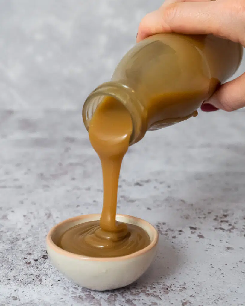 Creamy vegan caramel sauce being poured from a mini glass milk bottle into a small serving dish