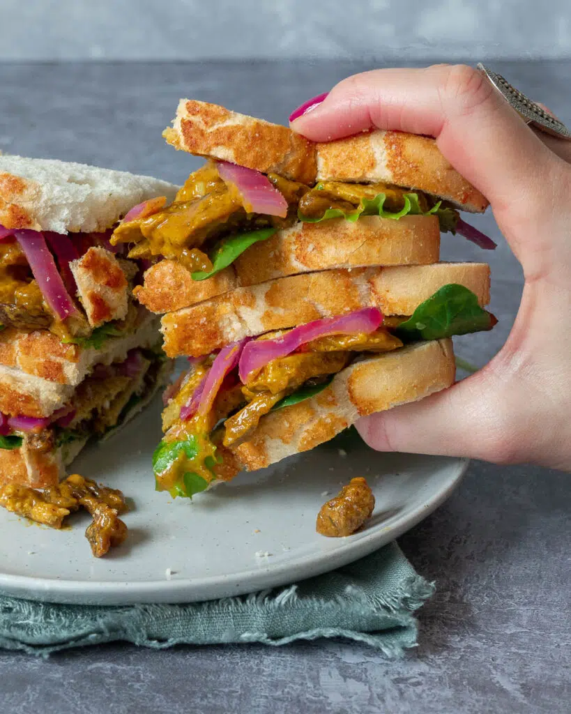 A colourful vegan coronation chicken sandwich cur in half, with crusty farmhouse bread, coronation chick'n, lettuce and pickled red onions