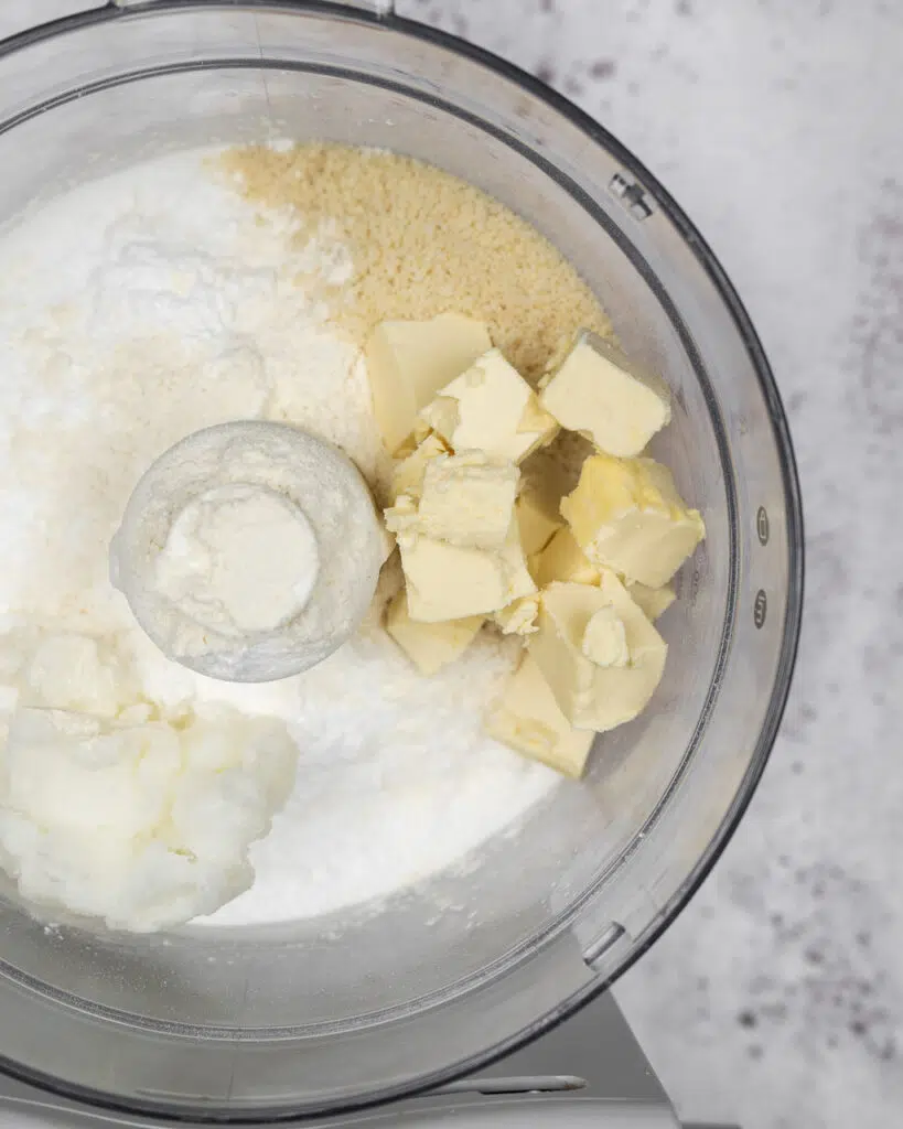 Flour, sugar, butter and oil in a food processor ready to be blended into a vegan shortcrust pastry