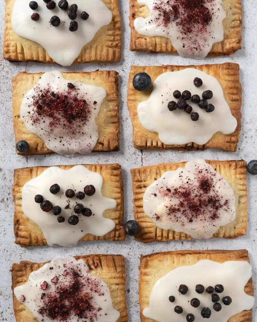 A top down view of a batch of blueberry vanilla vegan pop tarts, topped with icing and freeze dried blueberries.