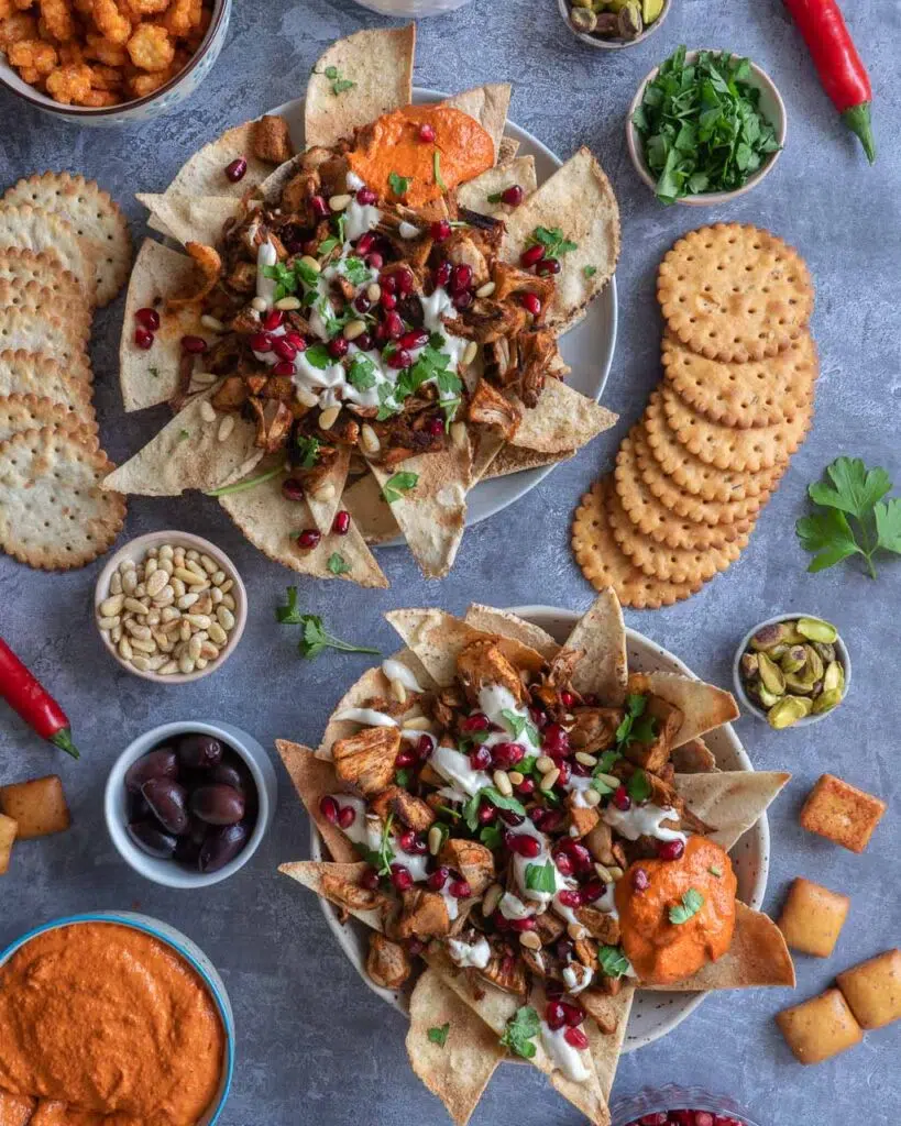 Two bowls of colourful jackfruit fatteh loaded with pitta nachos, spiced jackfruit, pomegranate, tahini sauce, pine nuts, muhammara dip and fresh parsley.