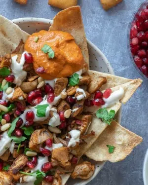 A close up of a colourful bowl of Middle Eastern Jackfruit Nachos loaded with pitta nachos, spiced jackfruit, pomegranate, tahini sauce, pine nuts, muhammara dip and fresh parsley.