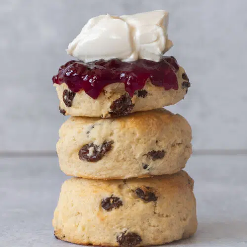 A stack of three fruit vegan scones topped with raspberry jam and vegan cream