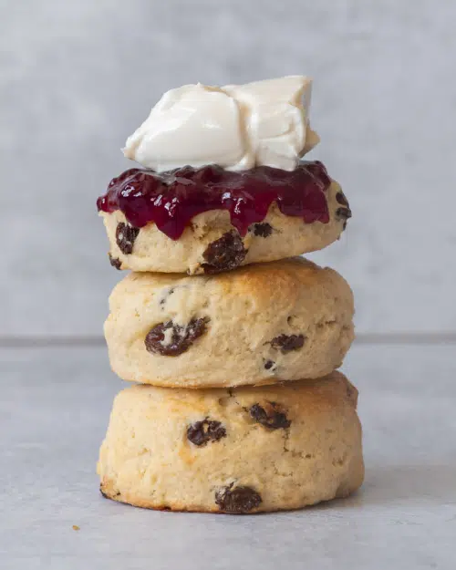 A stack of three fruit vegan scones topped with raspberry jam and vegan cream