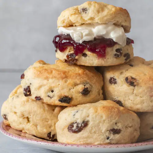 A plate piled high with vegan scones, the top one filled with vegan cream and jam