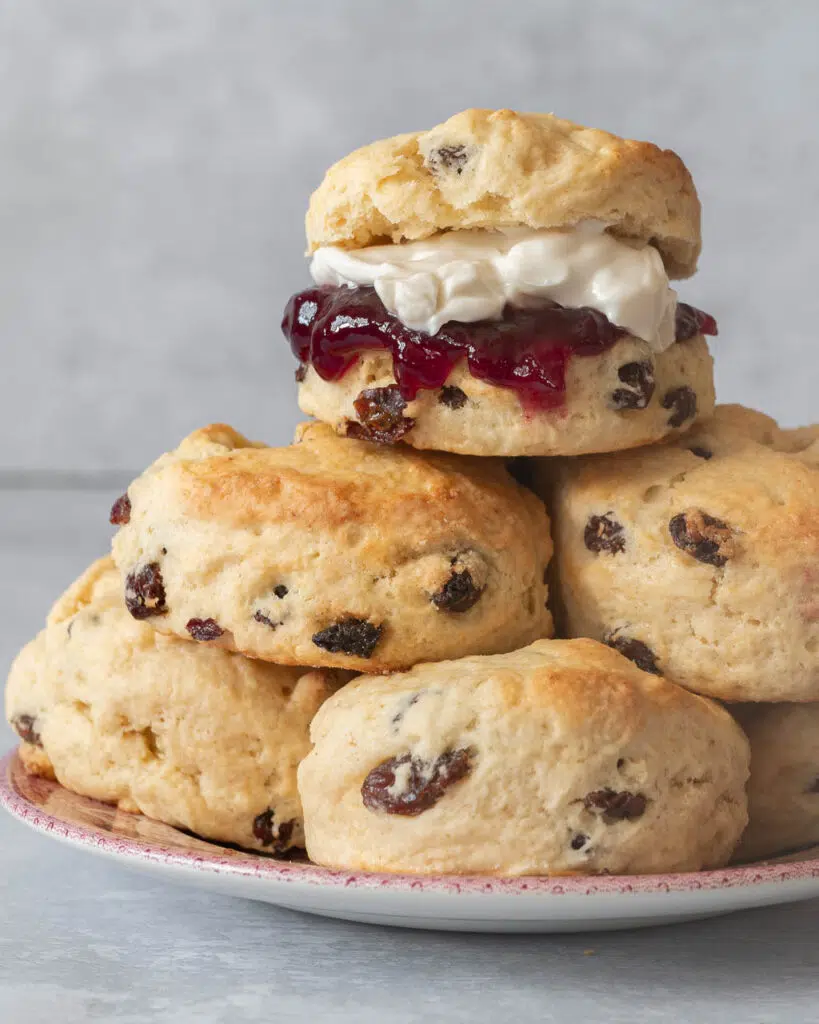 A plate piled high with vegan scones, the top one filled with vegan cream and jam