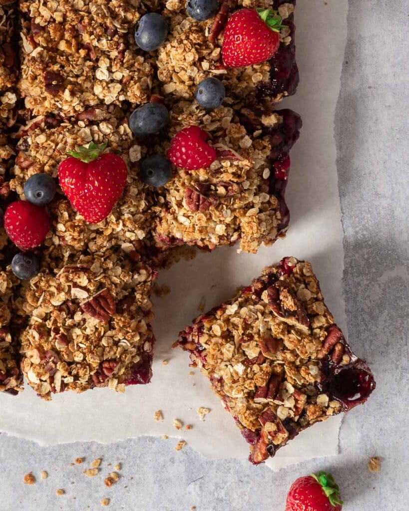 Top down photo of a tray of vegan crumble bars, cut into squares with one pulled out and decorated with fresh berries