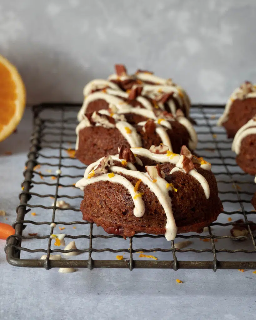 Carrot cake doughnuts sat on a cooling rack drizzled with tofu icing and sprinkled with chopped nuts