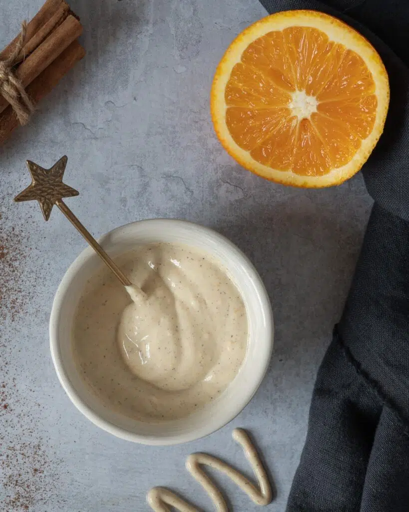 A bowl of creamy tofu icing with a star shaped gold spoon and an orange cut in half resting beside it