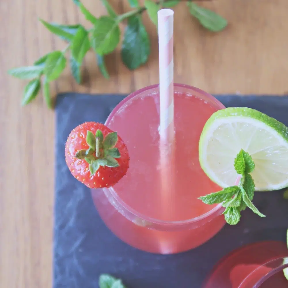 An icy pink gin cocktail adorned with a fresh strawberry, lime slice and mint leaves