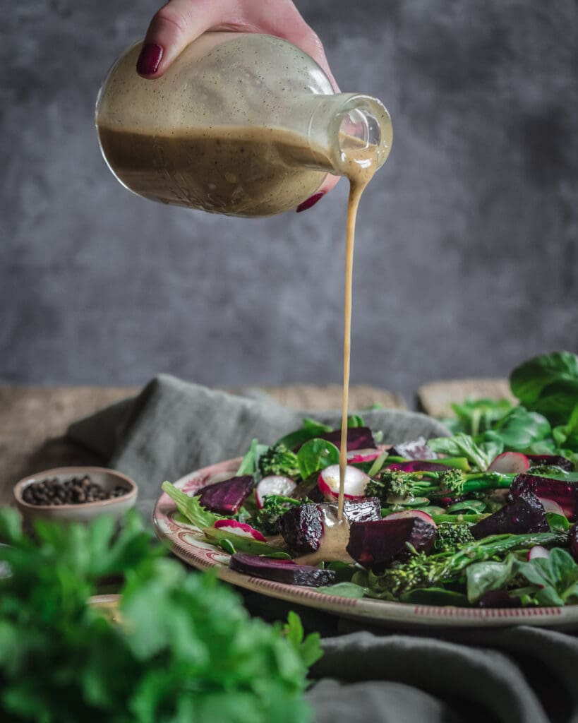 A platter of roasted vegetables being drizzled with healthy vegan salad dressing from a glass bottle.