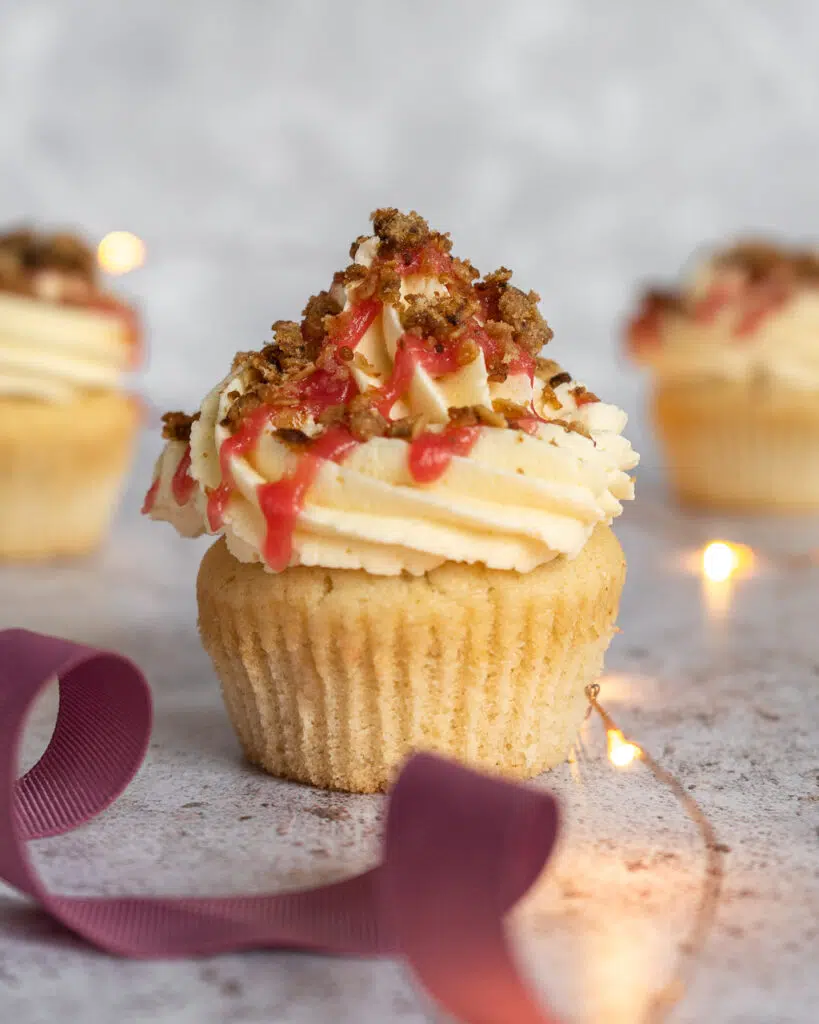 A pretty rhubarb crumble cupcake with vanilla sponge, vanilla buttercream, a zig zag of rhubarb compote and oat crumble topping