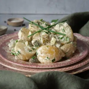 Vegan potato salad on vintage pink plates with chives on top. Sat on top of a green linen tea towel.