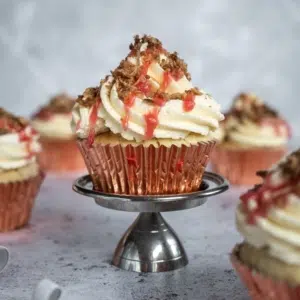 Vegan rhubarb crumble cupcakes in pink cupcake cases stood on a silver cake stand.