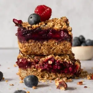 Summer berry crumble bars with a layer of golden oat crumble on the top and bottom, a middle layer of red summer berry jam and topped with fresh berries.