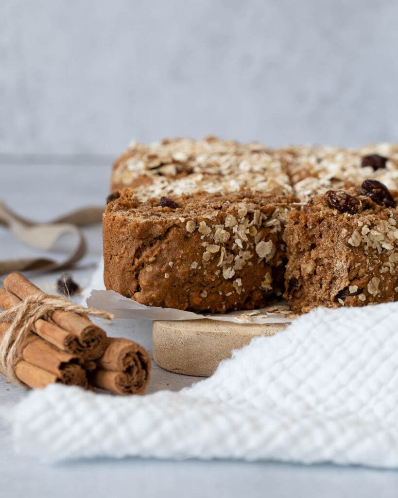 Cinnamon raisin cake bars on a wooden chopping board with a stack of cinnamon sticks in the foreground