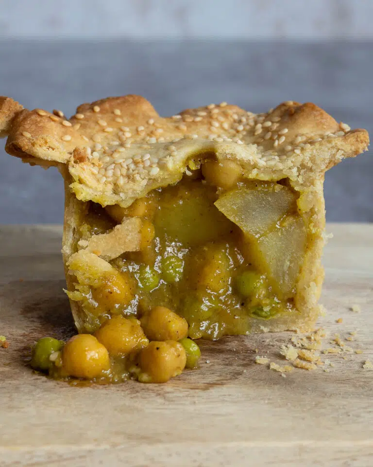 A curried chickpea and potato pie cut in half with a saucy filling spilling out onto a wooden board