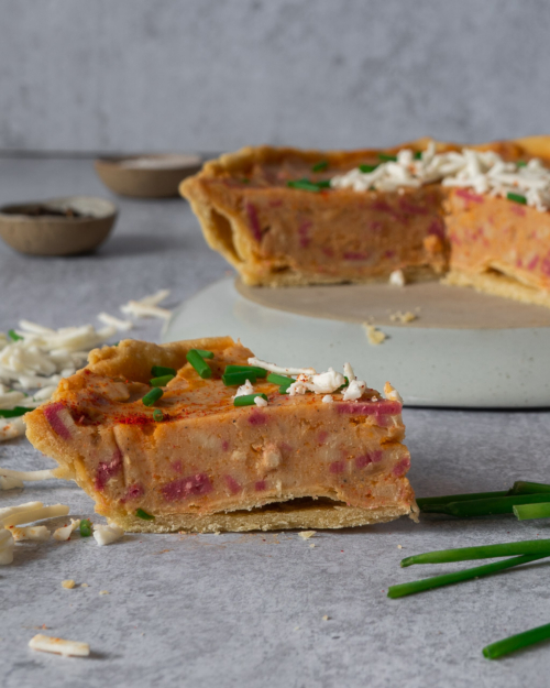 A chunky slice of vegan Quiche Lorraine sat on a worktop with grated vegan cheese and fresh chives sprinkled over it