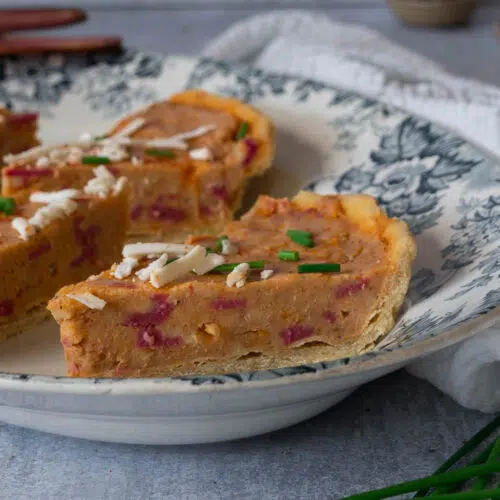 A serving dish with slices of vegan Quiche Lorraine on it, sprinkled with grated cheese and fresh chives