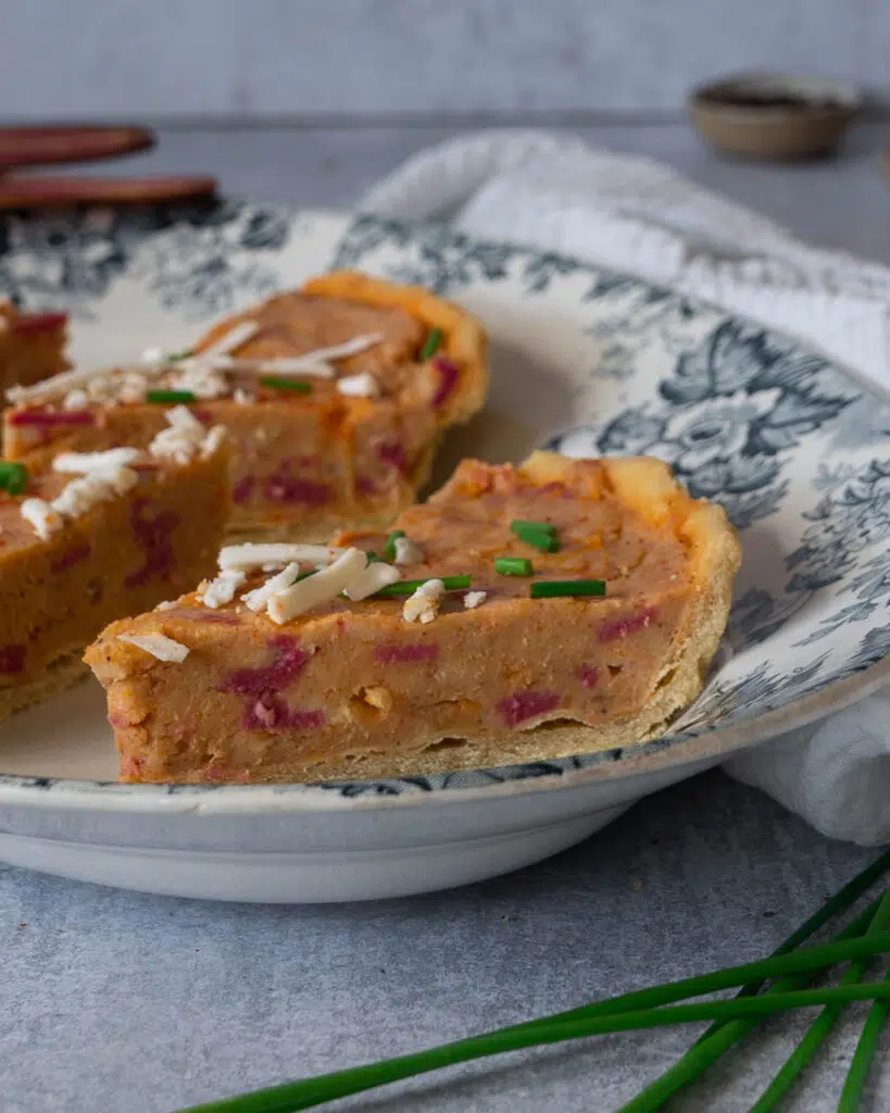 A serving dish with slices of vegan Quiche Lorraine on it, sprinkled with grated cheese and fresh chives