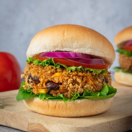 Homemade BBQ bean burgers in a crispy breadcrumb coating, in a soft bread roll with lettuce, tomato and thinly sliced red onion.