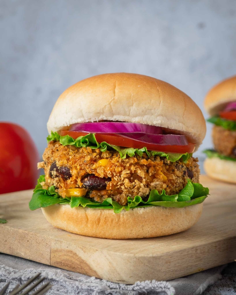 Homemade BBQ bean burgers in a crispy breadcrumb coating, in a soft bread roll with lettuce, tomato and thinly sliced red onion.