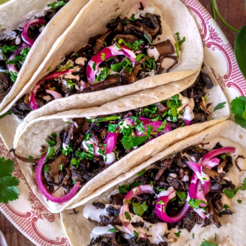 Colourful shredded mushroom carnitas in a soft tortilla with pickled red onions and fresh coriander