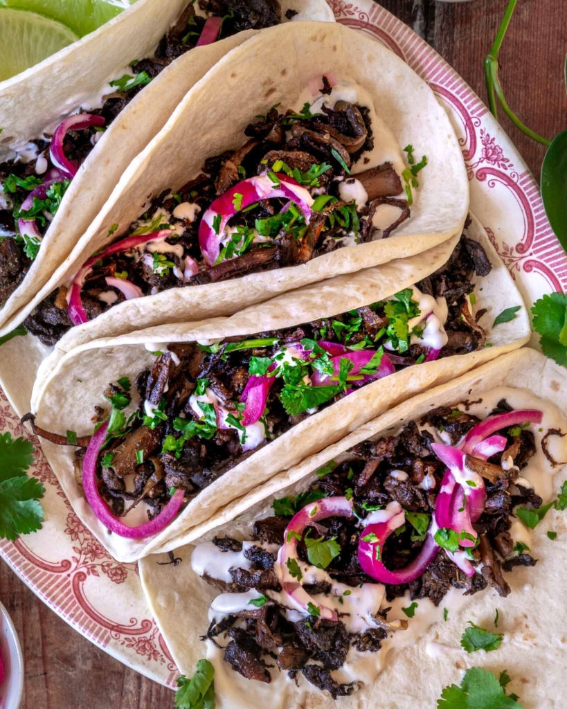Colourful shredded mushroom carnitas in a soft tortilla with pickled red onions and fresh coriander