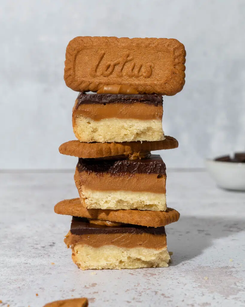 A stack of three Biscoff Billionaire's Shortbread with a trio of layers - vegan shortbread, biscoff spread and dark chocolate topped with a Lotus Biscoff biscuit