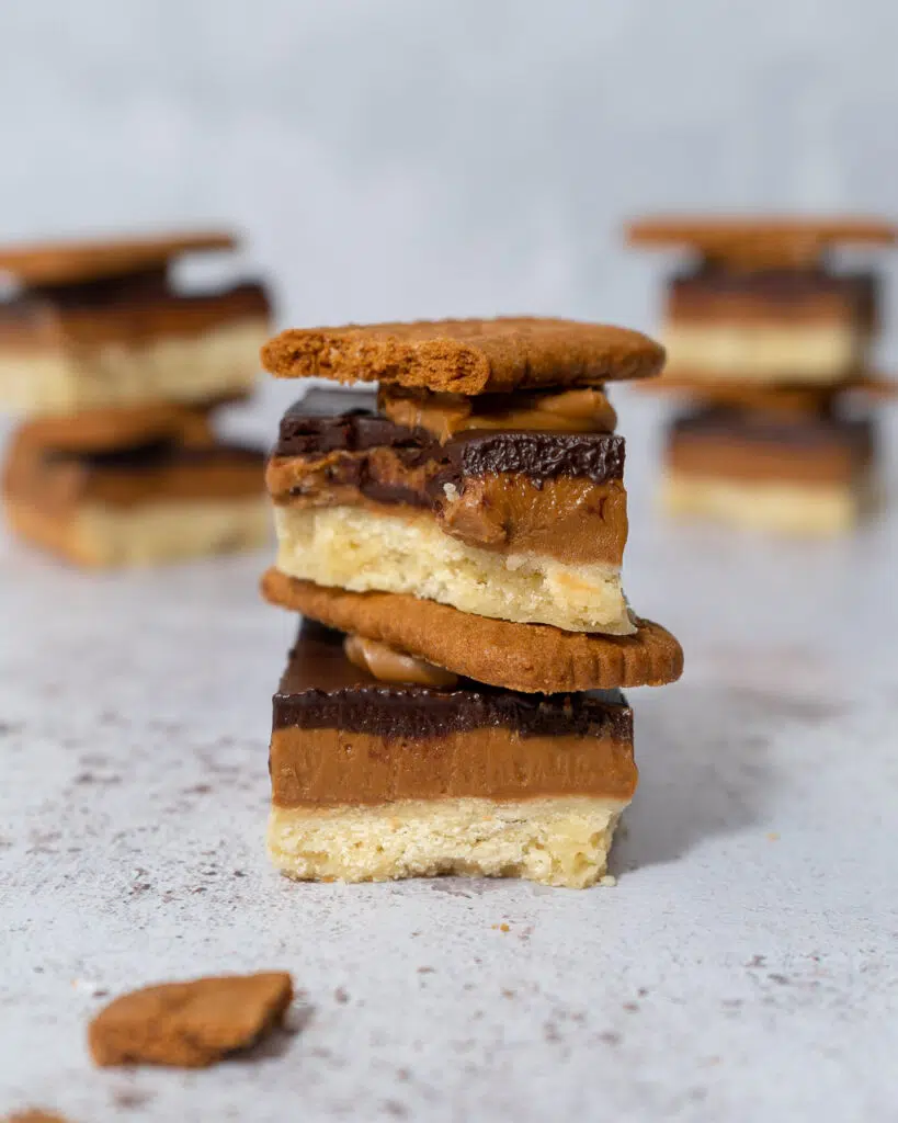 A stack of two Biscoff Billionaire's Shortbread with a trio of layers - vegan shortbread, biscoff spread and dark chocolate topped with a Lotus Biscoff biscuit