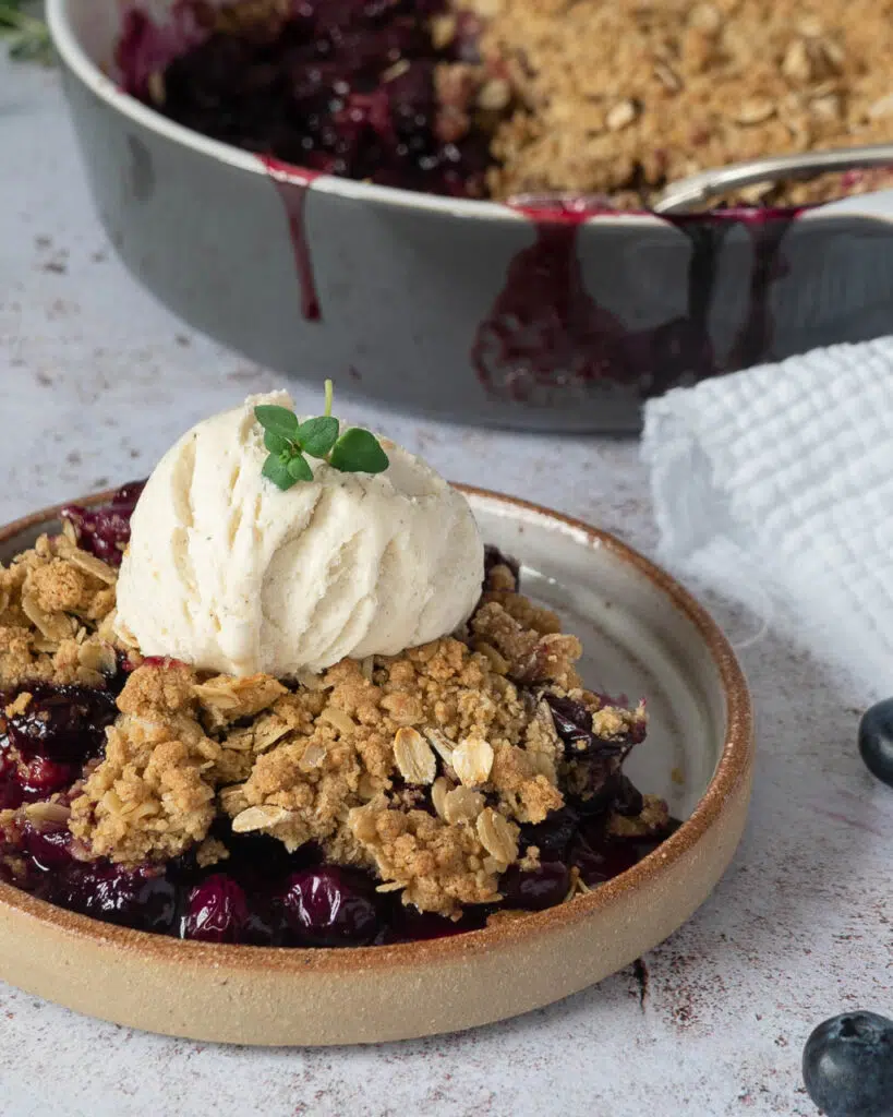 A plate of rich purple blueberry thyme crumble with a scoop of vegan vanilla ice cream on top