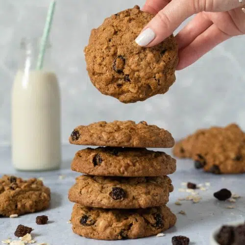 A stack of cinnamon raisin oat cookies with a bottle of oat milk