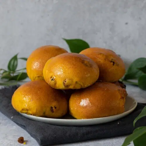 A plate of glossy golden yellow saffron buns studded with juicy sultanas