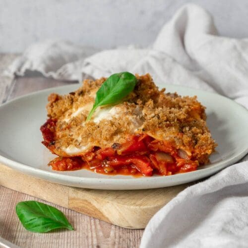 A plate of vegan vegetable lasagne with a garlic bread gratin topping and creamy white sauce