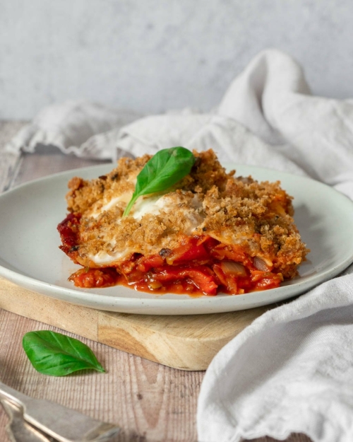 A plate of vegan vegetable lasagne with a garlic bread gratin topping and creamy white sauce