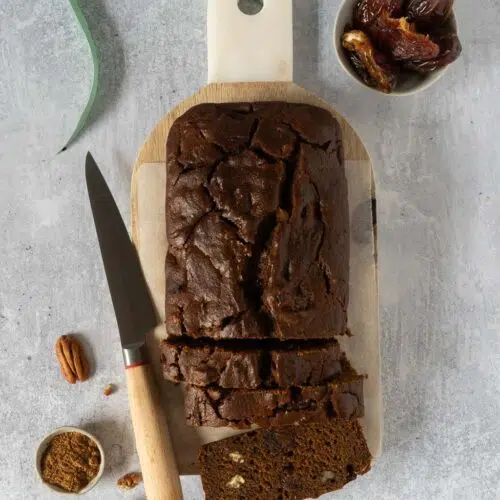 A rich sticky date cake on a wooden chopping board with three slices cut