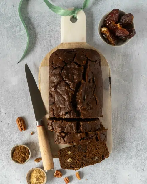A rich sticky date cake on a wooden chopping board with three slices cut