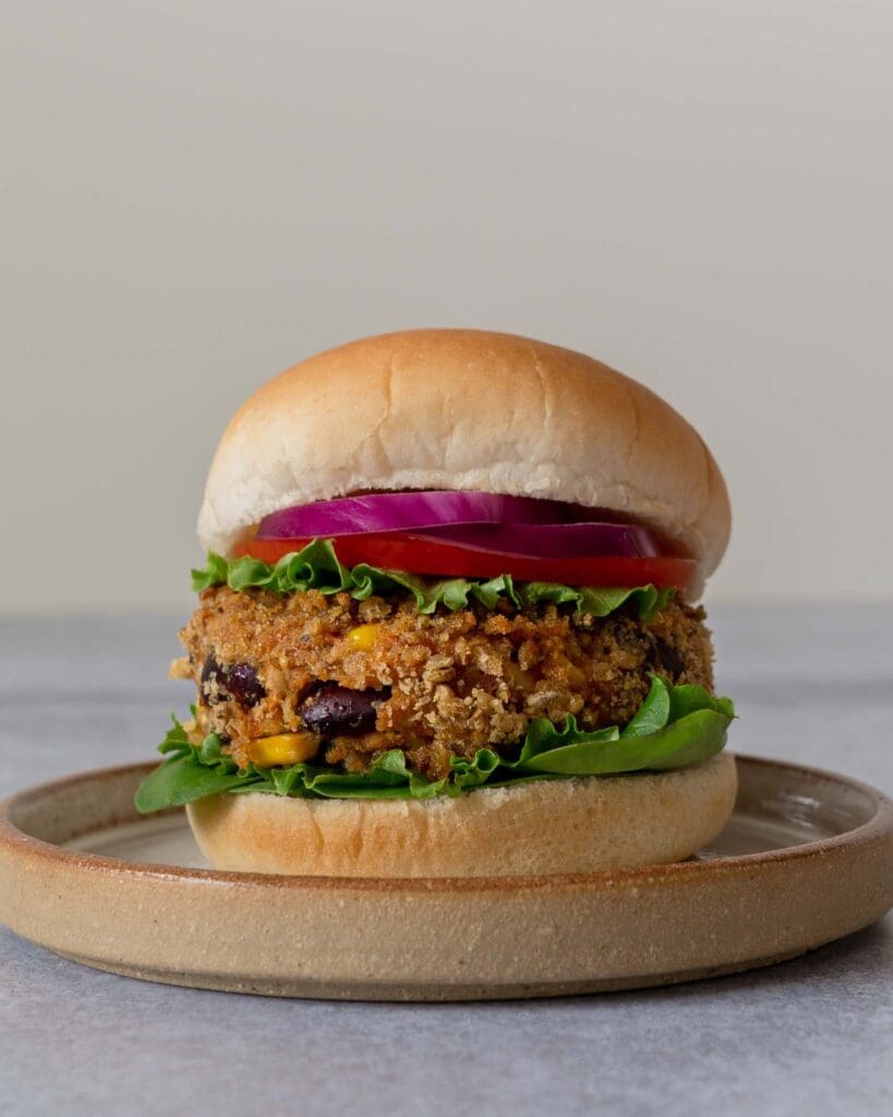 A homemade BBQ bean burger in a crispy breadcrumb coating, in a soft bread roll with lettuce, tomato and thinly sliced red onion.