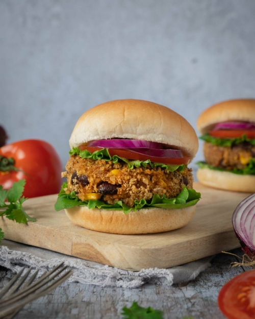 Homemade BBQ bean burgers in a crispy breadcrumb coating, in a soft bread roll with lettuce, tomato and thinly sliced red onion.