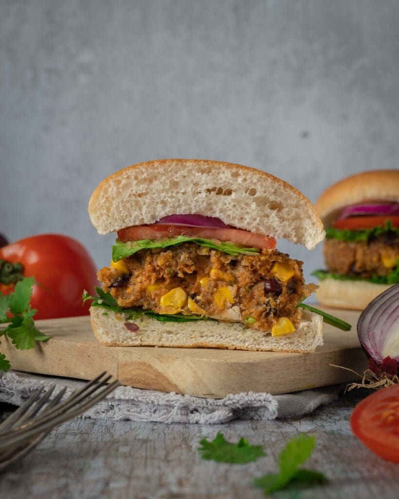 A homemade BBQ bean burger cut in half displaying the colourful and flavoursome interior, in a soft bread roll with lettuce, tomato and thinly sliced red onion.