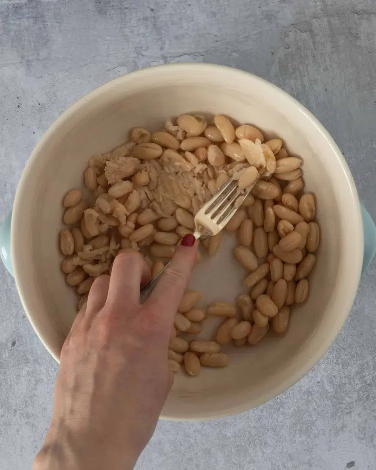 Cannellini beans being mashed with the back of a fork