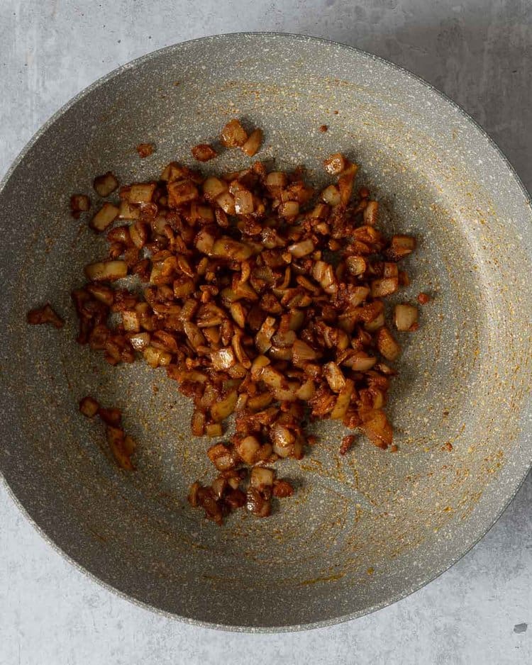 Diced onion being fried in spices in a non-stick frying pan