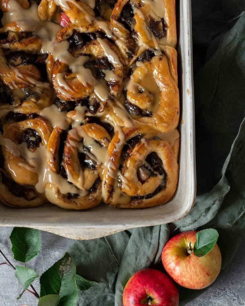 Sticky caramelised apple cinnamon buns in a baking dish topped with a drizzle of vegan caramel sauce.