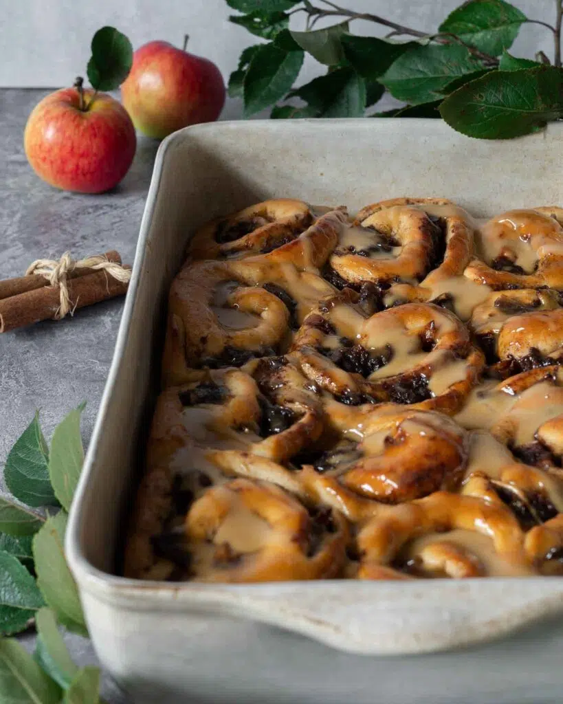 Sticky caramelised apple cinnamon buns in a baking dish topped with a drizzle of vegan caramel sauce.